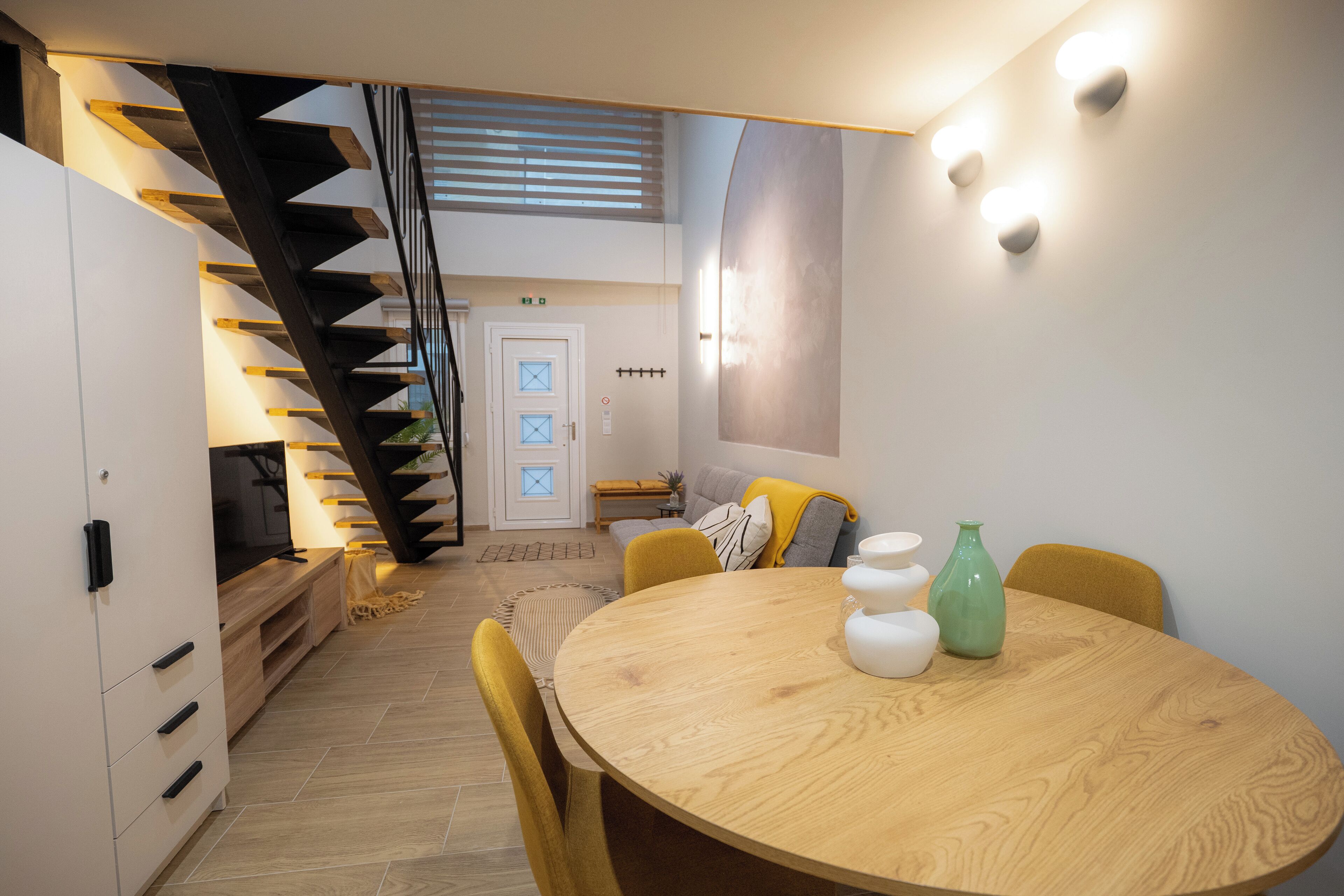 A modern interior with a wooden dining table, yellow chairs, a staircase, and a sofa with cushions.