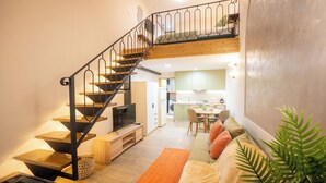 A modern interior with a wooden staircase, a sofa with cushions, a dining area, and a kitchen in the background. - Vayas Residences Agora (Trikala)
