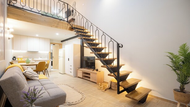 A modern living space with a staircase, a sofa, a coffee table, and a dining area. - Vayas Residences Agora (Trikala)