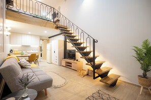 A modern living space with a staircase, a sofa, a coffee table, and a dining area. - Vayas Residences Agora (Trikala)