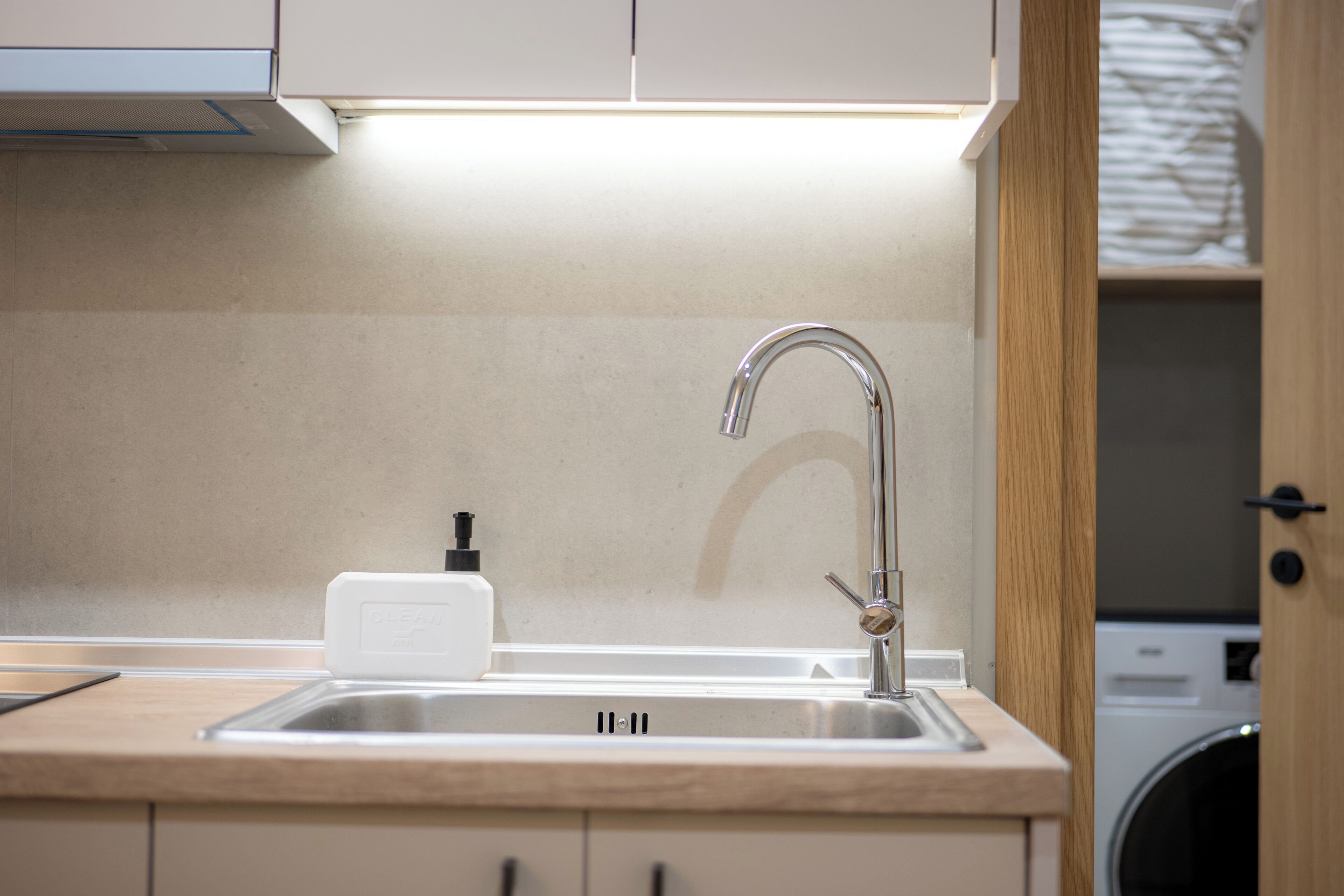 A modern kitchen with a stainless steel sink, a soap dispenser, and a washing machine in the background.