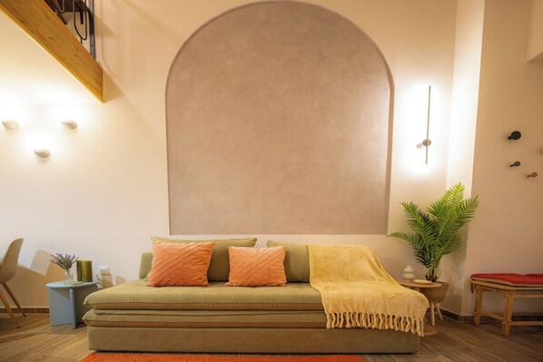 A cozy living room with a green sofa, orange cushions, a yellow throw blanket, and a large wall-mounted mirror. - Vayas Residences Agora (Trikala)
