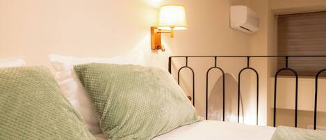 Een net opgemaakt bed met groene kussens, een wandlamp en een airconditioning.