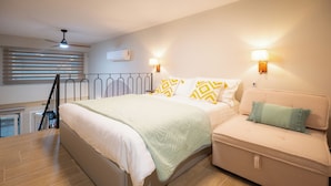 A bedroom with a bed, a sofa, a ceiling fan, and two wall-mounted lamps. - Vayas Residences Agora (Trikala)