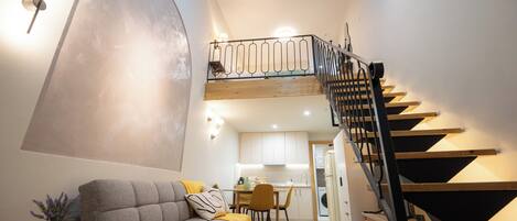 A modern living room with a sofa, a dining table, and a staircase leading to an upper level.