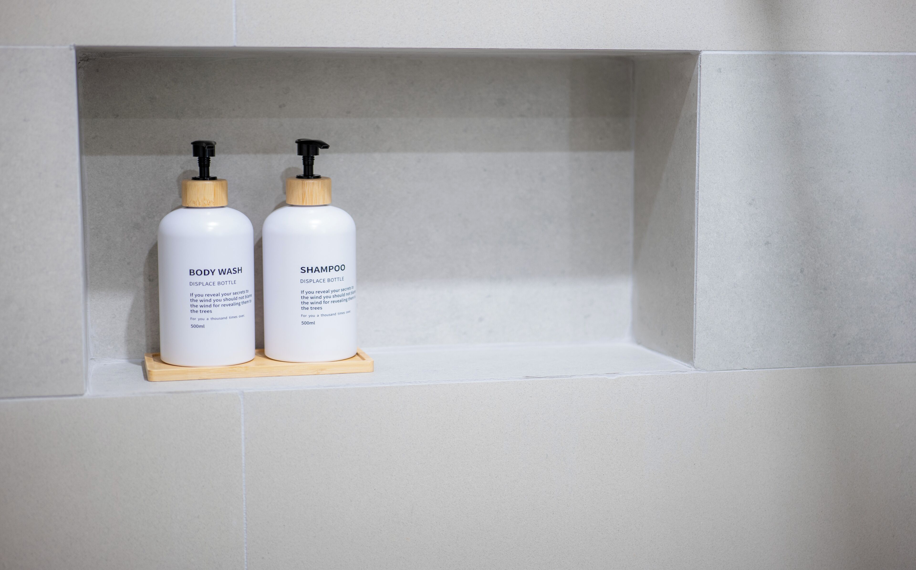 Two white bottles with black pumps on a wooden shelf against a tiled wall.