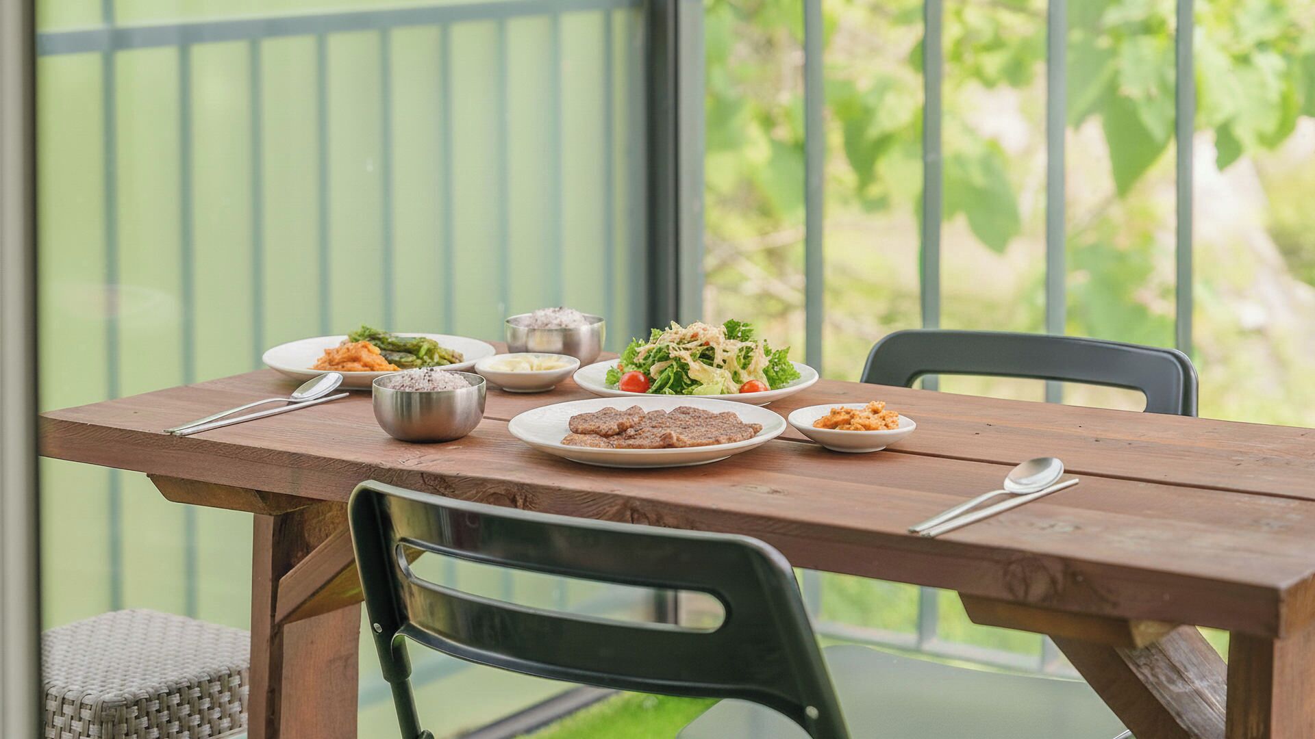 Una mesa de madera con platos de comida, un tazón y cubiertos.