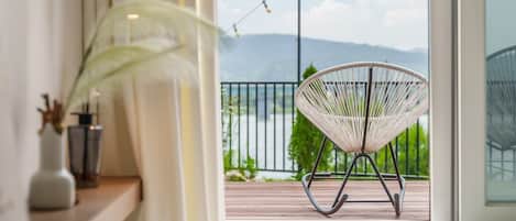 Un balcon avec un fauteuil en osier, une plante et une vue sur les montagnes.