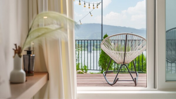 A balcony with a wicker chair, a plant, and a view of mountains.