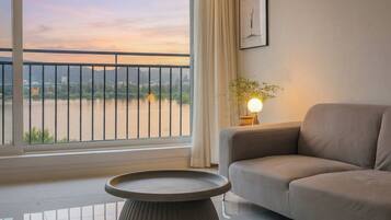 Una sala de estar moderna con sofá, una mesa redonda, una lámpara y vista a un río con un puente.