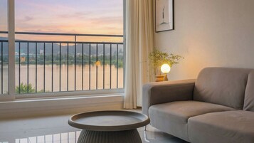 Una sala de estar moderna con sofá, una mesa redonda, una lámpara y vista a un río con un puente.