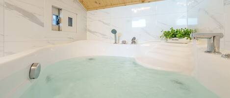 A modern bathroom with a large bathtub, a shower area, and a potted plant on the sink.