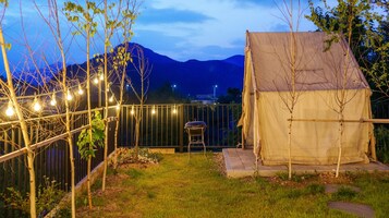 Um quintal com churrasqueira, luzes de festa e uma tenda.