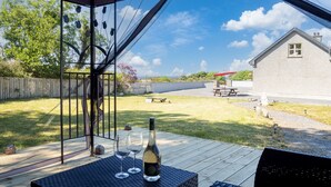 A covered patio with a table, two wine glasses, and a bottle of wine. - Whispering Meadows, Renvyle your perfect escape (Renvyle)