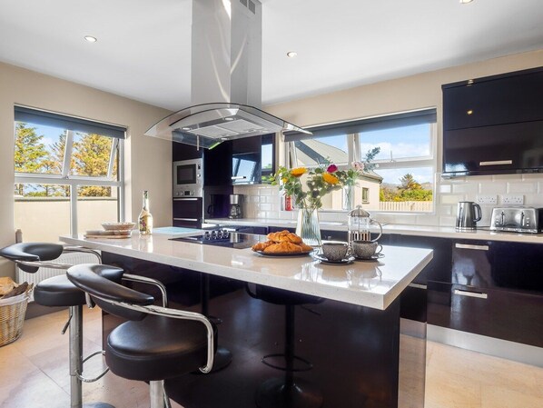 A modern kitchen with a large island, bar stools, and a view of the outdoors.