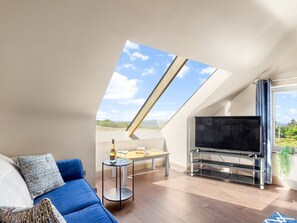 A modern living room with a TV, sofa, and dining area under a sloped ceiling with a skylight.