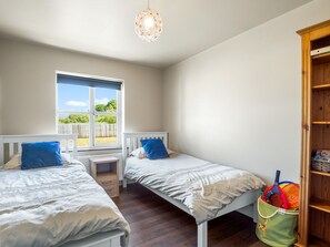 A bedroom with two beds, a window, a bedside table, and a wooden bookshelf.