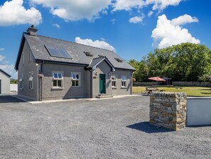 A two-story building with a stone facade, a green door, and a gravel driveway. - Whispering Meadows (Renvyle)