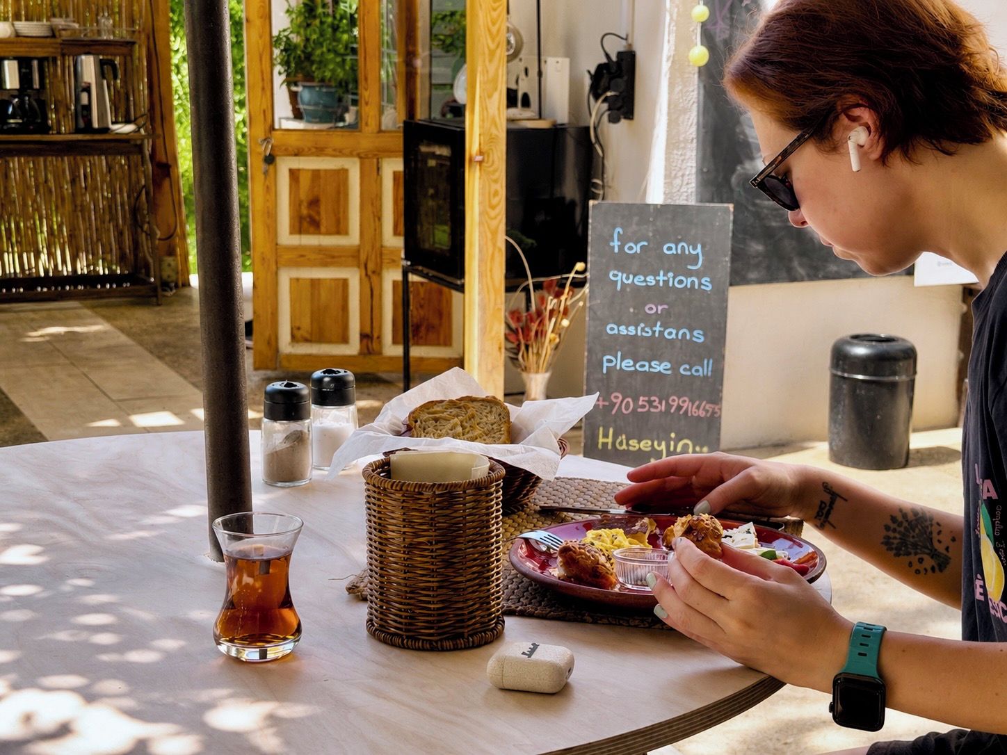 A person seated at a table with a meal, a sign with a phone number, and a basket with bread.