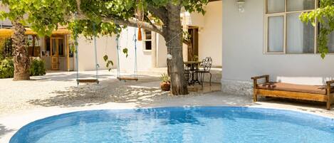 A swimming pool with a wooden deck, a bench, and a table with chairs.