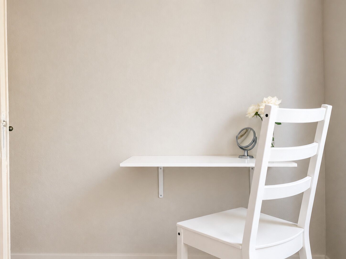 A white chair with a backrest, a white table, and a small mirror on the table.