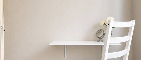 A white chair with a backrest, a white table, and a small mirror on the table.