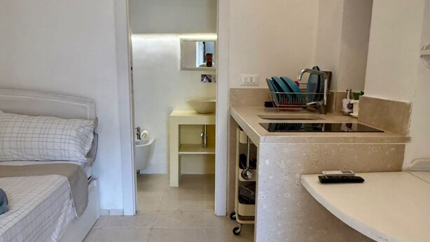 Um quarto com cama, um banheiro pequeno com pia e espelho, e uma cozinha compacta com bancada e micro-ondas.