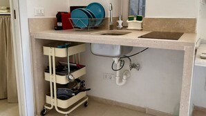 Uma cozinha com pia, escorredor de louça, cafeteira e suporte para secar a louça.