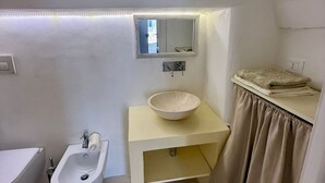 Casa de banho com lavatório, espelho, porta-toalhas e uma pequena janela.