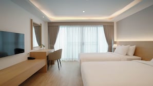 Une chambre d’hôtel avec un grand lit, un bureau avec une chaise, un téléviseur fixé au mur et une grande fenêtre avec des rideaux.