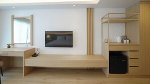 Une chambre moderne avec un bureau en bois, un lit avec une tête de lit, une armoire et un banc intégré.