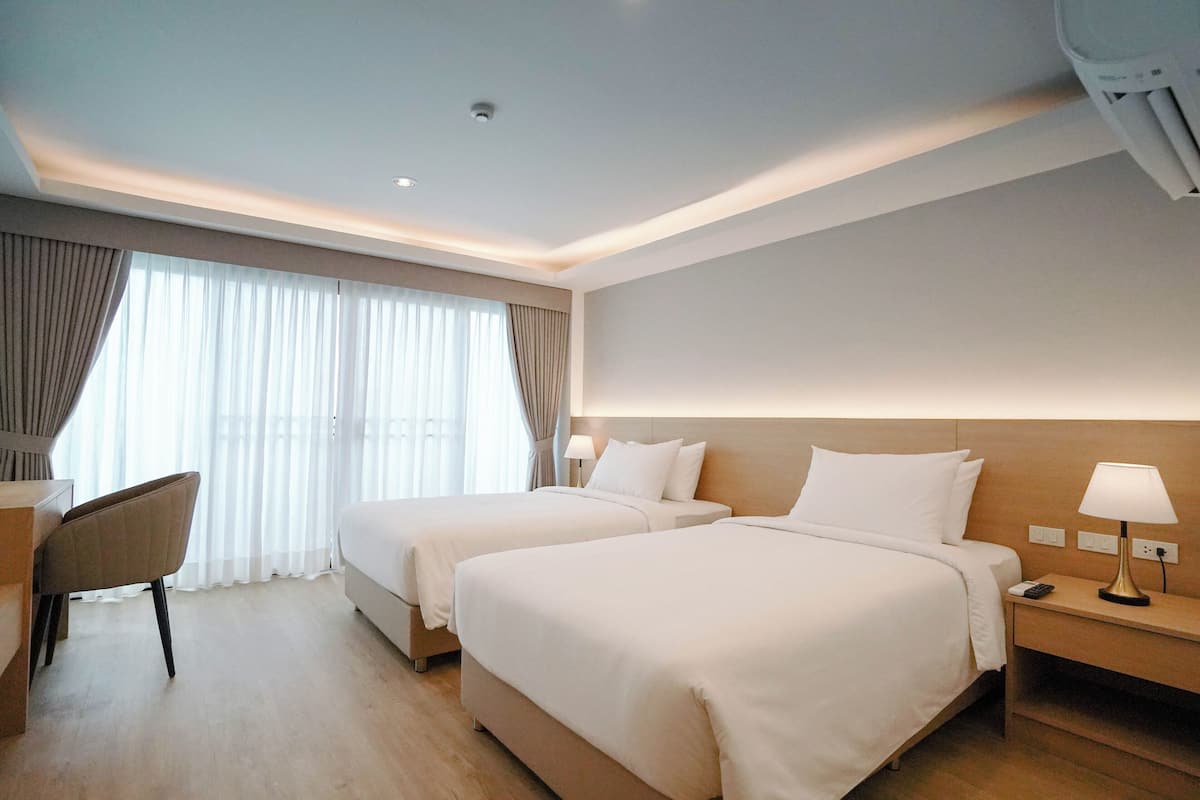 Ein Hotelzimmer mit zwei Betten, einem Schreibtisch, einem Stuhl und einem Nachttisch mit Lampe.