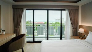 Une chambre d’hôtel avec un grand lit, un bureau, une chaise, une table de chevet avec une lampe et un balcon offrant une vue sur la ville.