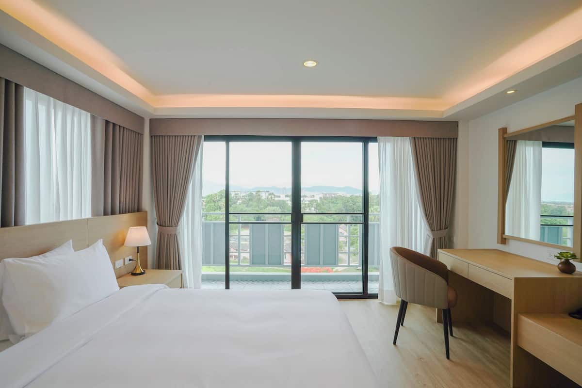 Ein Hotelzimmer mit einem großen Bett, einem Schreibtisch und Blick auf einen Balkon.