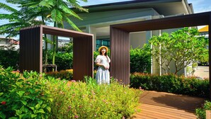 Un espace extérieur moderne doté d’une terrasse en bois, entouré d’une végétation luxuriante et de plantes en fleurs.