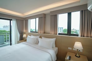Una habitación de hotel con una cama grande, dos mesitas de noche con lámparas, un control remoto y vistas a la ciudad a través de amplias ventanas.