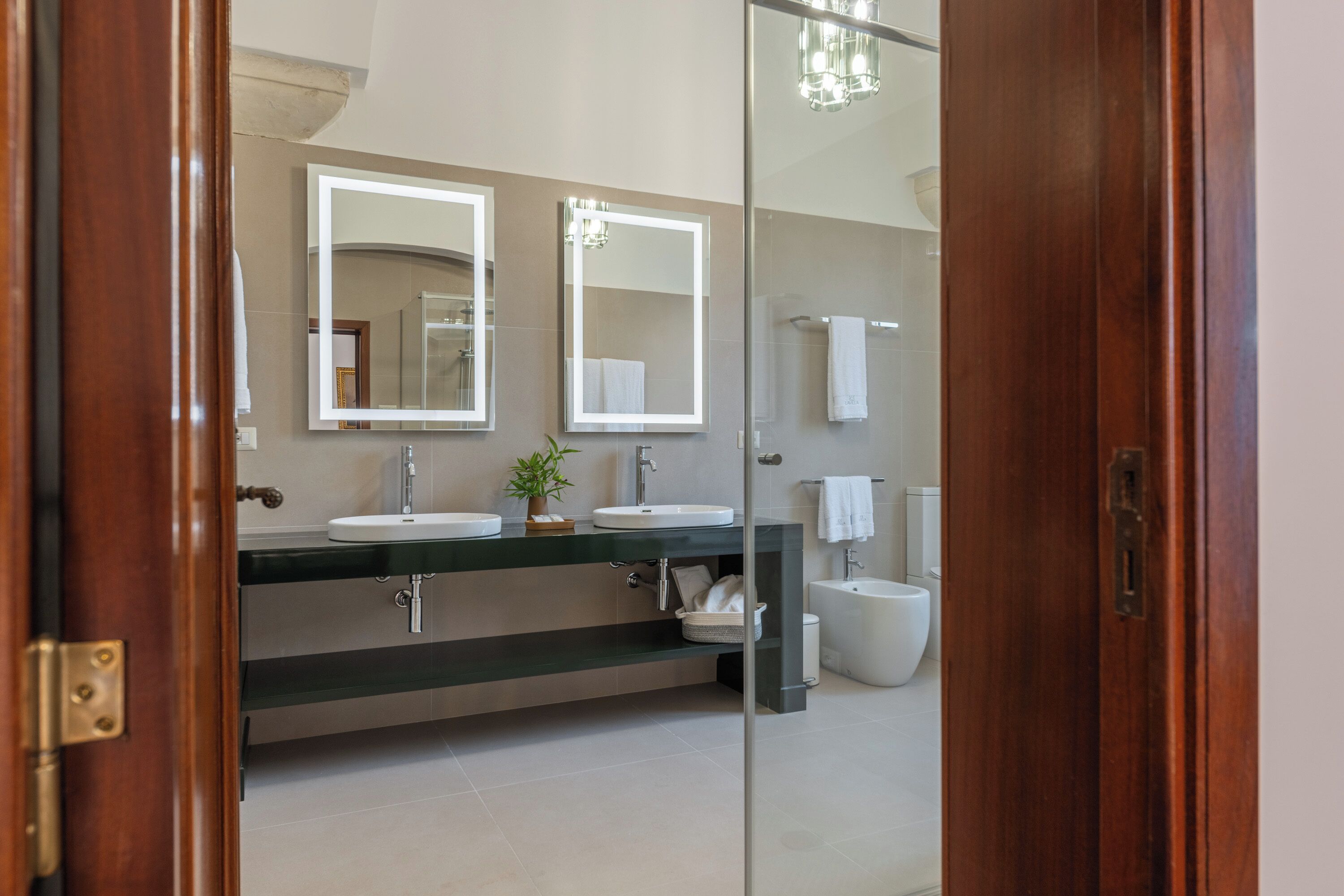 A modern bathroom with two sinks, a large mirror, and a glass partition.