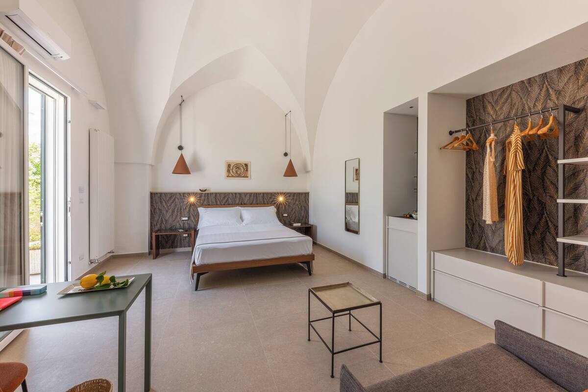 A modern bedroom with a bed, bedside tables, a small table, and a seating area.
