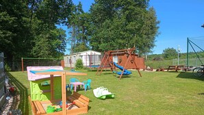 Un jardin avec une cabane en bois, une balançoire et un toboggan.