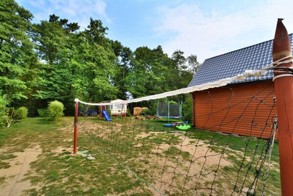 A fenced backyard with a volleyball net, a wooden playhouse, and a slide.