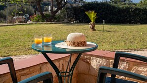 A table with two glasses of orange juice, a woven hat, and a potted plant in a garden setting. - Comfortable Apartment with Shared Pool & Beautiful Garden (Hersonissos)