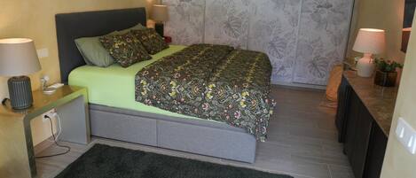 Un dormitorio con cama, mesitas de noche, cómoda y un panel decorativo con estampado floral.