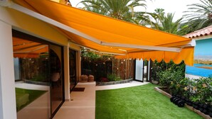 Un patio techado con césped artificial, cerca de madera y vista al mar.