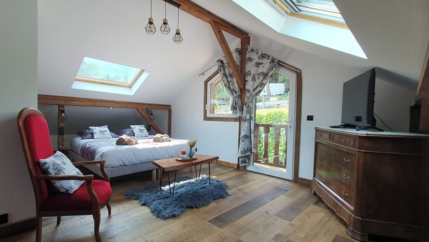 A bedroom with a skylight, a bed with pillows, a red chair, a wooden dresser, and a television.