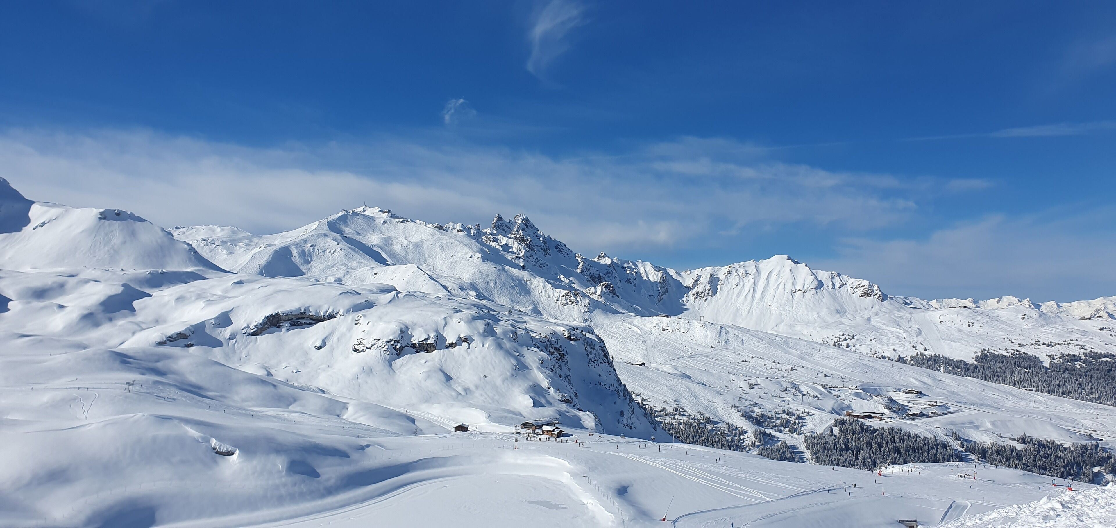 Eine verschneite Berglandschaft mit Skipisten und einer kleinen Siedlung am Fuße.