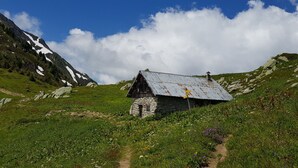 A rustic stone building with a metal roof, surrounded by a mountainous landscape and a clear sky.