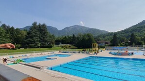 A swimming pool with multiple lanes, surrounded by greenery and mountains in the background.