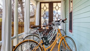 Un porche con bicicletas estacionadas, piso de madera y vista a los árboles a través de una ventana.