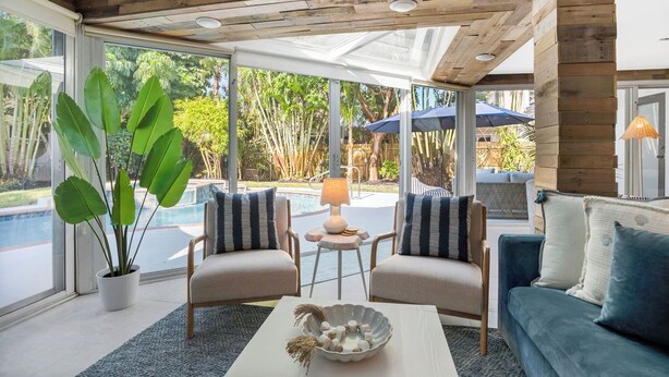 A modern living room with a glass ceiling, large windows, a pool, and outdoor furniture. - Pool/Spa & Walk to the Beach Ping Pong Billiards (Palm Beach Shores)