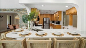 A modern kitchen with white cabinetry, a central island, and a dining area with a round table set for six. - Pool/Spa & Walk to the Beach Ping Pong Billiards (Palm Beach Shores)